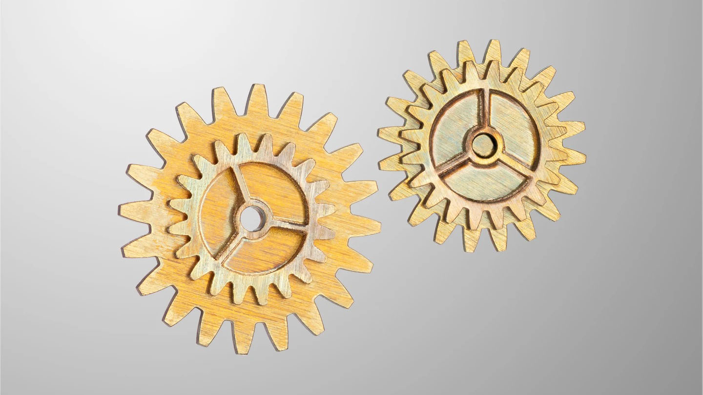 Two small precision-cut metal gears with intricate spokes and teeth are displayed against a light background, illustrating microscale fabrication or machining.