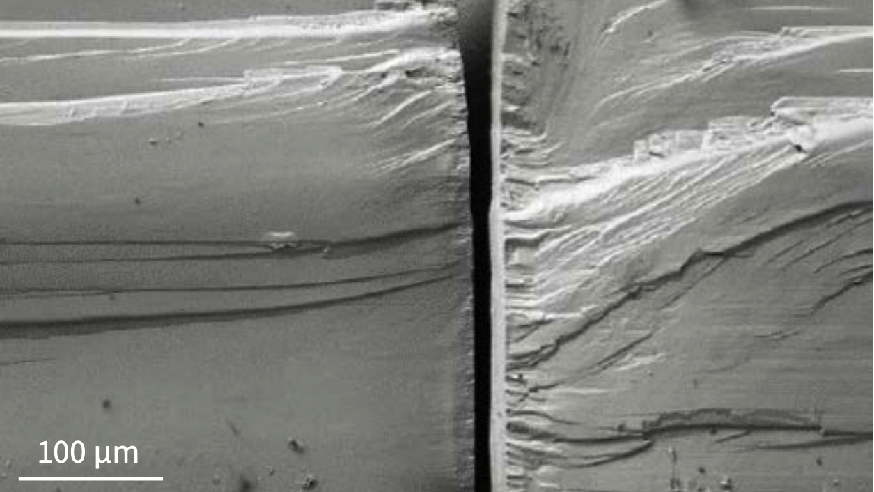 Scanning electron microscope (SEM) images show a textured titanium alloy surface with layered microscale patterns created by laser irradiation, including a magnified inset highlighting fine surface features and scale measurements.  Close-up of a metal cardiovascular stent with an intricate lattice structure mounted on a catheter against a dark background.  Scanning electron microscope (SEM) images show cross-sectional views of layered material structures with visible fracture patterns and delamination featu