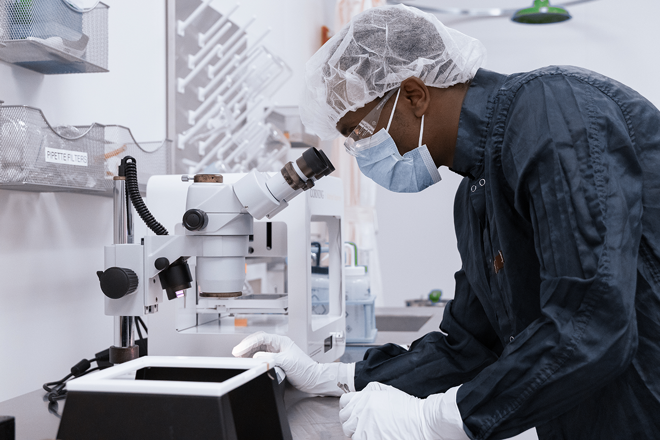 scientist in cleanroom looking through a microscope