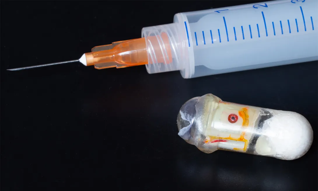 Prototype of an &quot;exploding&quot; capsule next to a syringe. The capsule can deliver medications that are typically only effective if injected.
